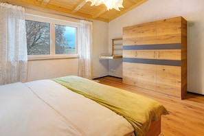 A bedroom with a bed, a wardrobe, a window with curtains, and a wooden ceiling.