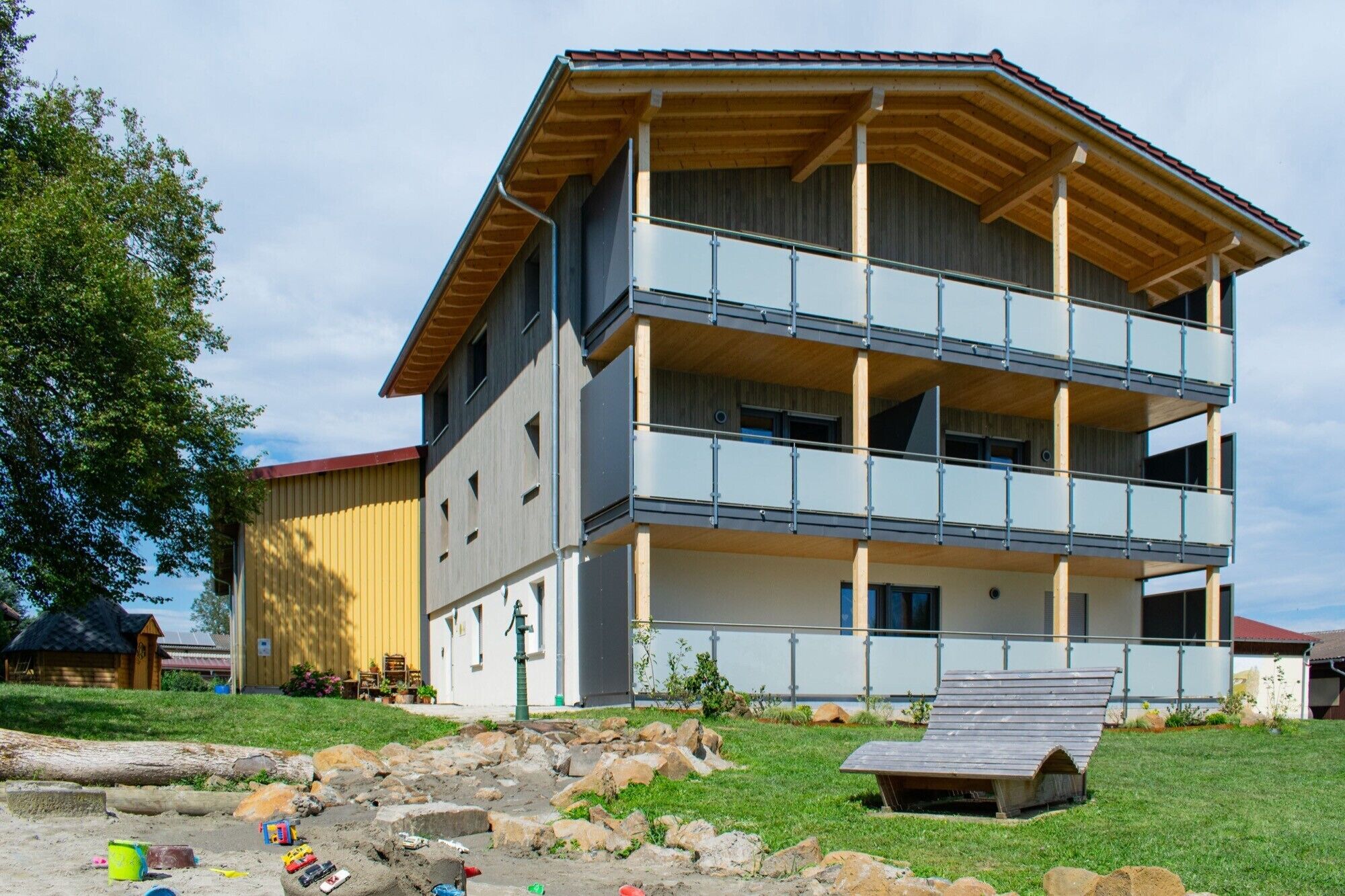 Um edifício de vários andares com varandas, um deck de madeira e um gramado.