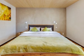 Une chambre à coucher avec une tête de lit en bois, un lit recouvert d’une couverture verte, deux lampes de chevet et un luminaire fixé au mur.