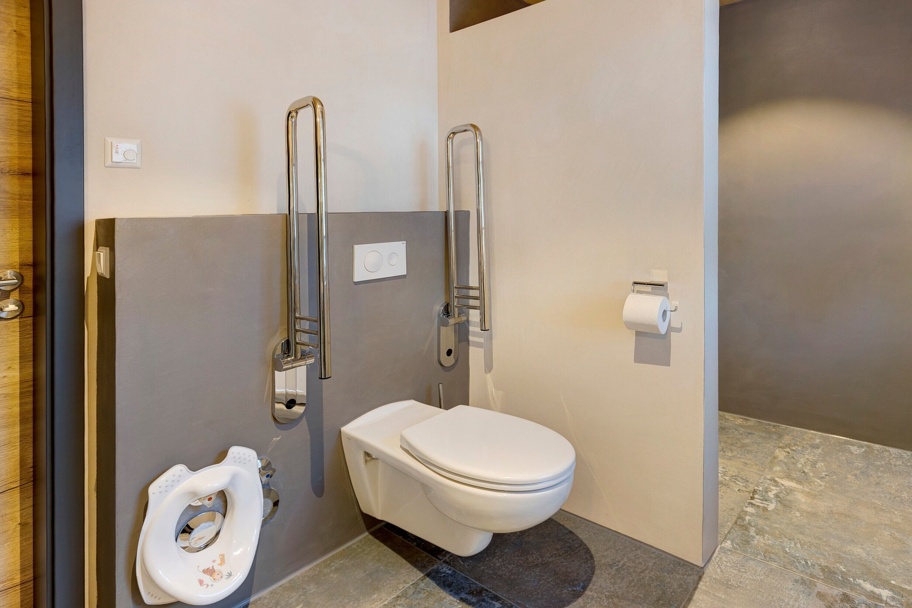 A modern bathroom with a toilet, grab bars, and a roll of toilet paper.