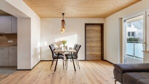 A dining area with a wooden table and chairs, a hanging light fixture, and a view through a glass door. - Apartment 'Ebbi' with Balcony, Accessible, Dogs Allowed, BBQ Hut & Infrared Cabin (Donaueschingen)