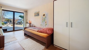 A bedroom with a bed, a wardrobe, a painting, and a view through the glass door. - Apartment 'Freiraum' with Mountain View, Private Terrace and Wi-Fi (Weiler Simmerberg)