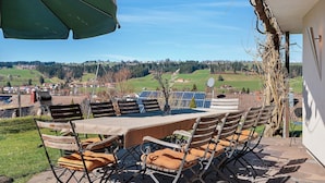 An outdoor patio with a table and chairs, a green umbrella, and a view of a rural landscape. - Apartment 'Freiraum' with Mountain View, Private Terrace and Wi-Fi (Weiler Simmerberg)