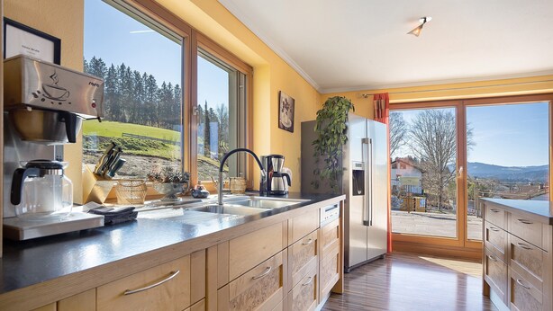 A modern kitchen with a coffee machine, sink, and large windows offering a view of the outdoors.