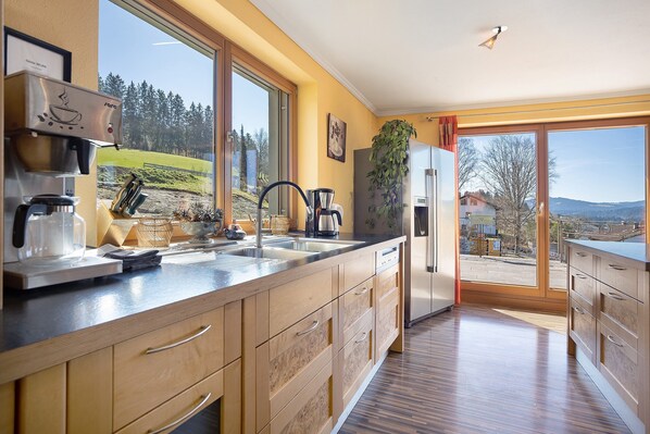 A modern kitchen with a coffee machine, sink, and large windows offering a view of the outdoors. - Apartment 'Lichtblick' with Mountain View, Balcony and Wi-Fi (Weiler Simmerberg)