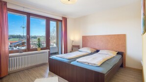 Une chambre avec deux lits, une fenêtre avec des rideaux, un radiateur et une vue sur l’extérieur.