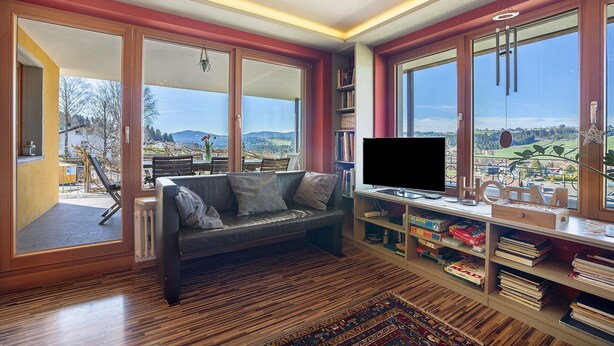 A modern living room with a sofa, TV, bookshelves, and large windows offering a view of the outdoors. - Apartment 'Lichtblick' with Mountain View, Balcony and Wi-Fi (Weiler Simmerberg)