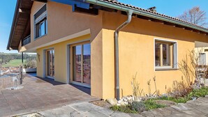 A modern house with a yellow facade, large windows, and a stone pathway.
