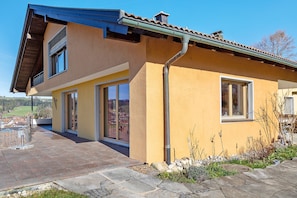 A modern house with a yellow facade, large windows, and a stone pathway.