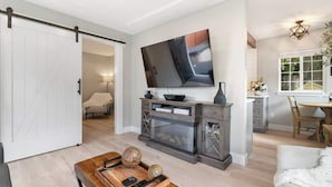 Una sala de estar con un televisor de pantalla plana grande, una mesa de centro de madera y un divisor corredizo que da a otra habitación.