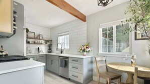 Una cocina moderna con armarios blancos, una viga de techo de madera y una zona de comedor con una mesa redonda y sillas.