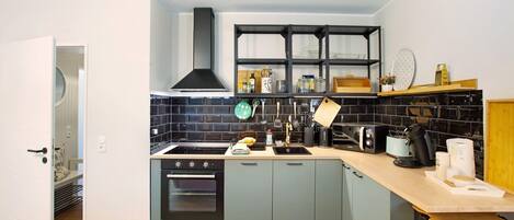 A compact kitchen with a built-in oven, a sink, and a black range hood.