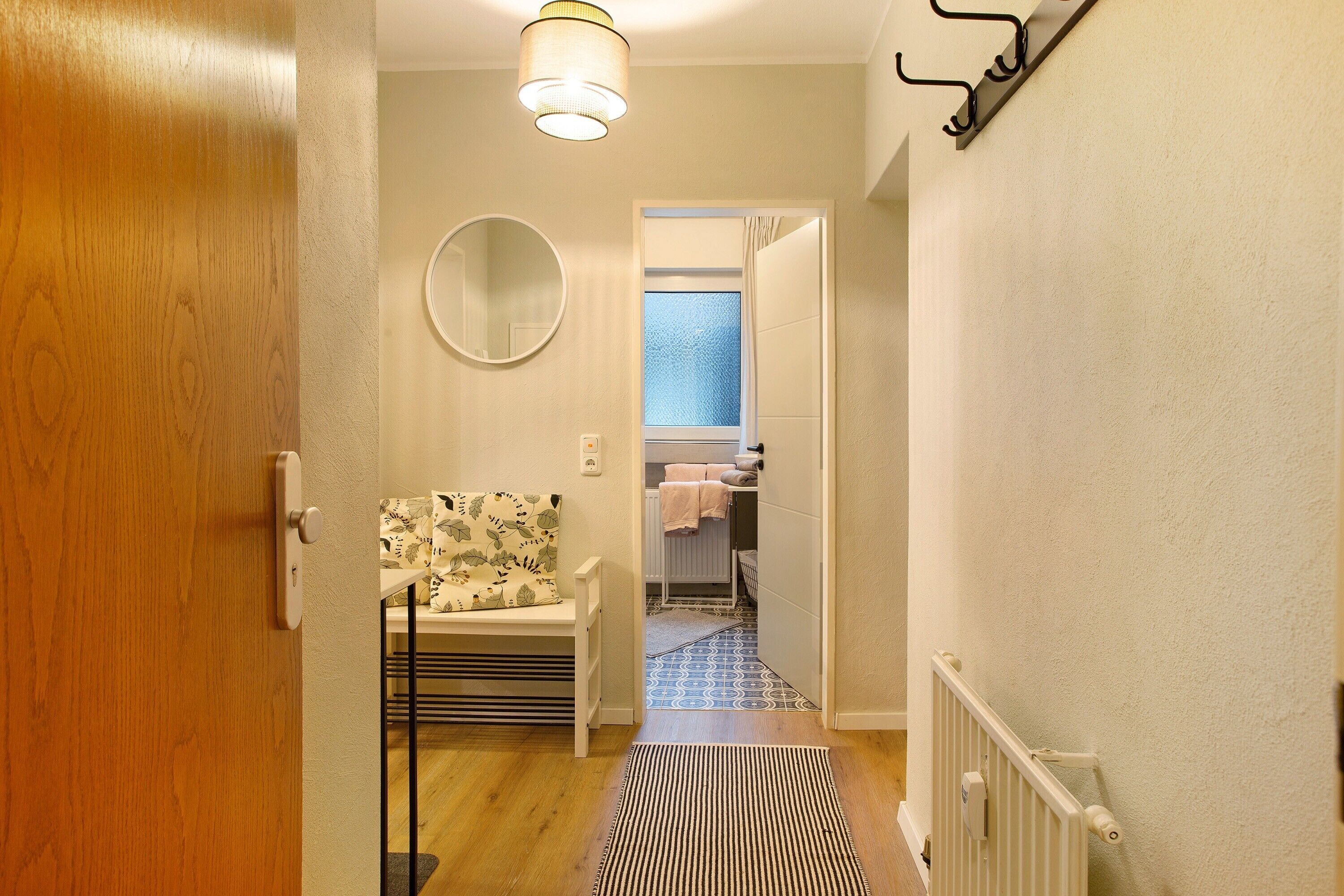 A hallway with a wooden door, a radiator, a patterned bench, a mirror, and a patterned floor.