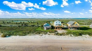 Une propriété située sur la côte, comprenant deux maisons, l’une bleue et l’autre jaune, qui offrent une vue sur une plage de sable et un paysage verdoyant.