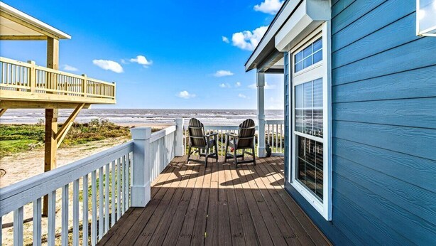Une terrasse en bois avec deux chaises et une table, donnant sur une plage.