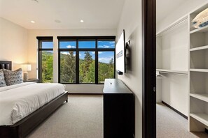 A bedroom with a bed, a TV, a wardrobe, and a large window with a view of trees and hills. - Modern Condo minutes from Beaver Creek! Basecamp14 (Avon)