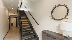 Een trap met een donkere leuning die uitkomt op een plateau, een spiegel aan de muur en een kast met lades.