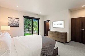 Une chambre à coucher comprenant un lit, une commode, un téléviseur et une porte-fenêtre coulissante donnant sur un balcon.