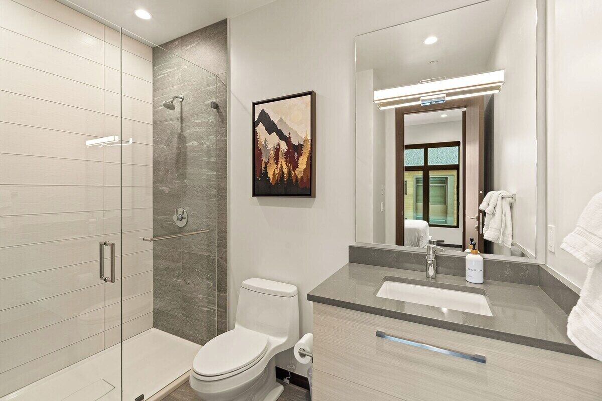 A modern bathroom with a glass-enclosed shower, a toilet, a sink, and a large mirror.