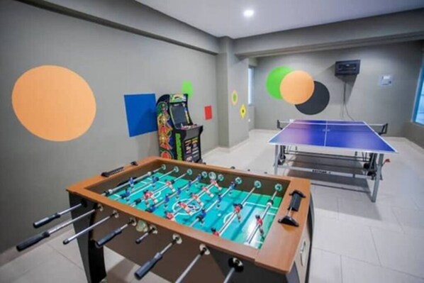 Een kamer met een tafelvoetbaltafel, een pingpongtafel en een tafelvoetbaltafel in de hoek.