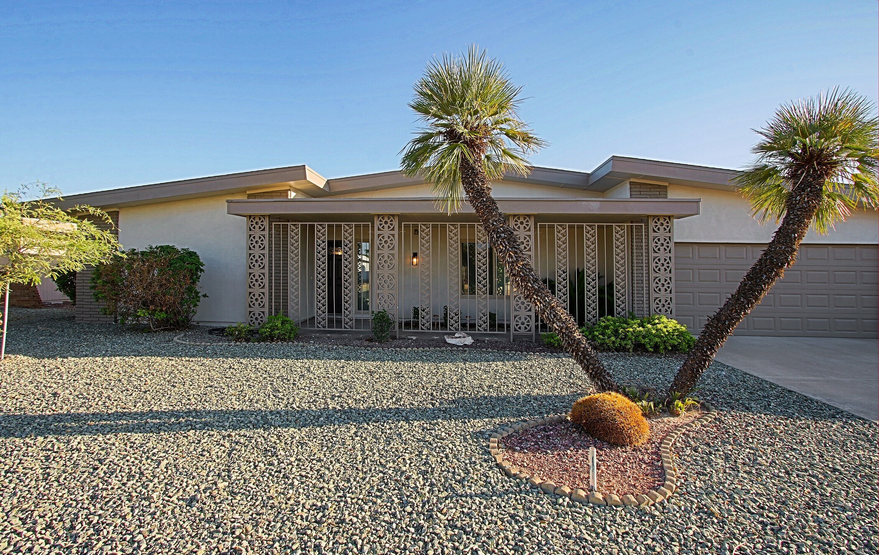 A modern house with a driveway, palm trees, and a decorative garden.