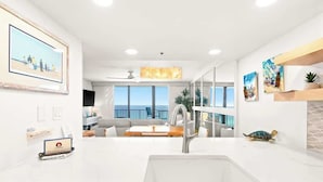 A modern kitchen with a large window, a dining area with a view, and a living room with a sofa and a coffee table.