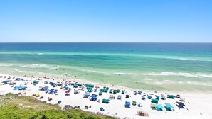 A beach with numerous umbrellas and beach chairs, a clear blue sky, and the ocean.