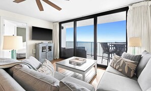 A modern living room with a large TV, grey sofas, a coffee table, and a balcony with a view of the sea. - One Seagrove Place 0802 (Santa Rosa Beach)