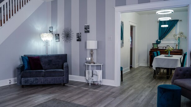 Un salon moderne avec un canapé gris, une petite table d’appoint et un coin repas agrémenté de rideaux turquoise et d’un lustre.