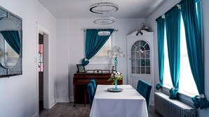 Une salle à manger avec un piano, des rideaux turquoise et une nappe blanche.
