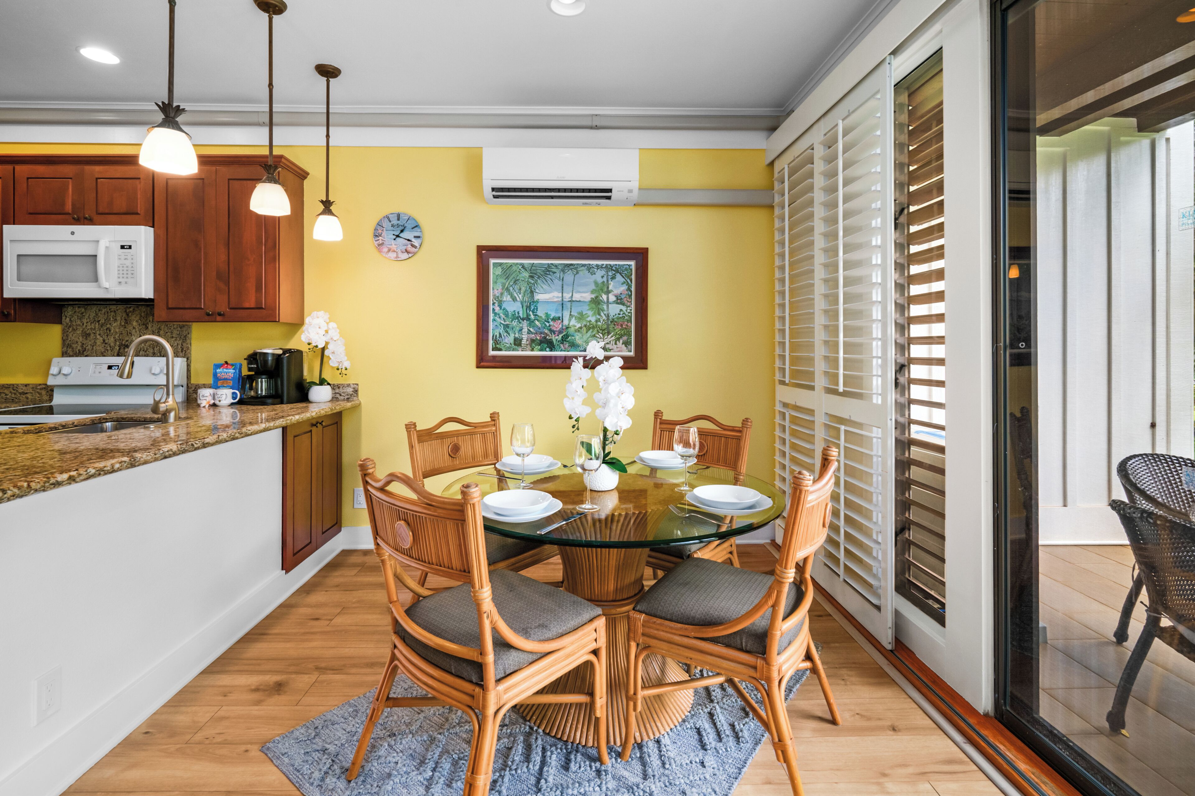 A dining area with a round glass table, wooden chairs, and a kitchen in the background.