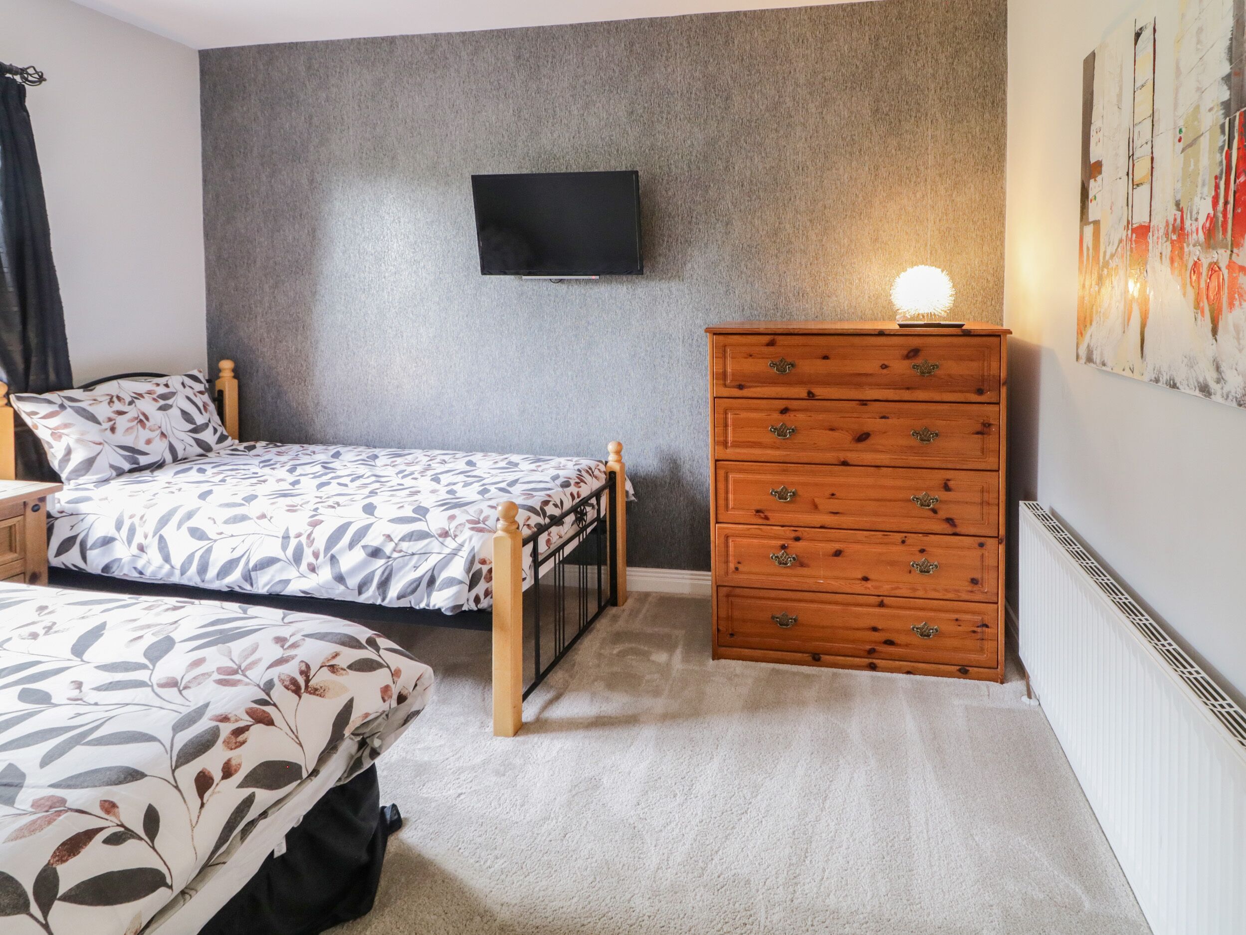 Ein Schlafzimmer mit Bett, Kommode, Fernseher an der Wand und Heizkörper.