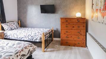 Ein Schlafzimmer mit Bett, Kommode, Fernseher an der Wand und Heizkörper.