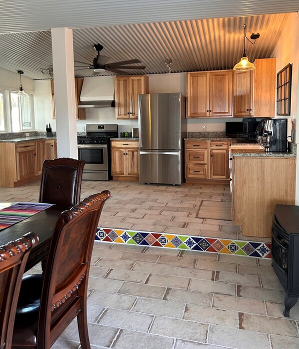 A kitchen with wooden cabinets, a stainless steel refrigerator, a stove, and a dining area with a table and chairs. - Mucho Gusto: Luxury 2br2ba, 3 Minutes from BBNP (Terlingua)