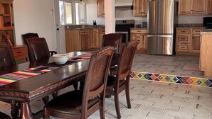 A spacious kitchen with wooden cabinets, a stainless steel refrigerator, and a dining area with a large wooden table and chairs. - Mucho Gusto PLUS Casita: 3br 3ba, 2.4 miles from BBNP (Terlingua)
