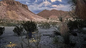 A desert landscape with rocky terrain, sparse vegetation, and distant mountains under a partly cloudy sky. - Mucho Gusto PLUS Casita: 3br 3ba, 2.4 miles from BBNP (Terlingua)