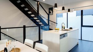 A modern kitchen with a central island, a glass staircase, and a dining area with white chairs. - Bright 3BR 3 Level Townhouse Port Melbourne (Port Melbourne)