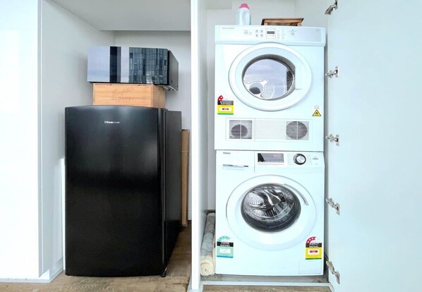 Une petite buanderie avec un réfrigérateur noir et un appareil combiné lave-linge et sèche-linge.