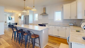 Una cocina moderna con una isla grande, taburetes de bar, iluminación colgante y armarios blancos.