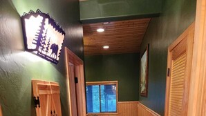 Un couloir aux murs recouverts de lambris en bois, une fenêtre avec des stores et une porte dotée d’une poignée.