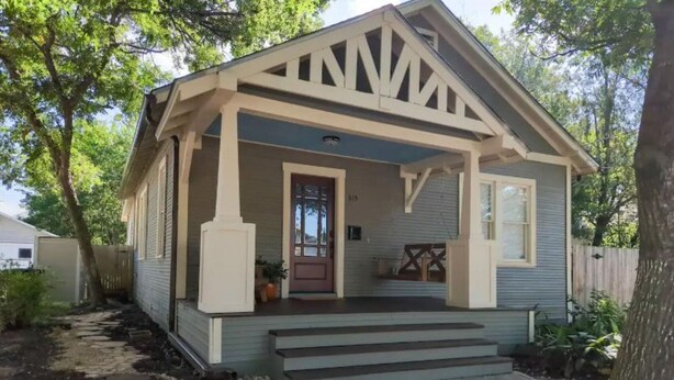 Ein kleines, eingeschossiges Haus mit Veranda, Eingangstür und einer kleinen Grünfläche mit einem Weg und einem Blumentopf.