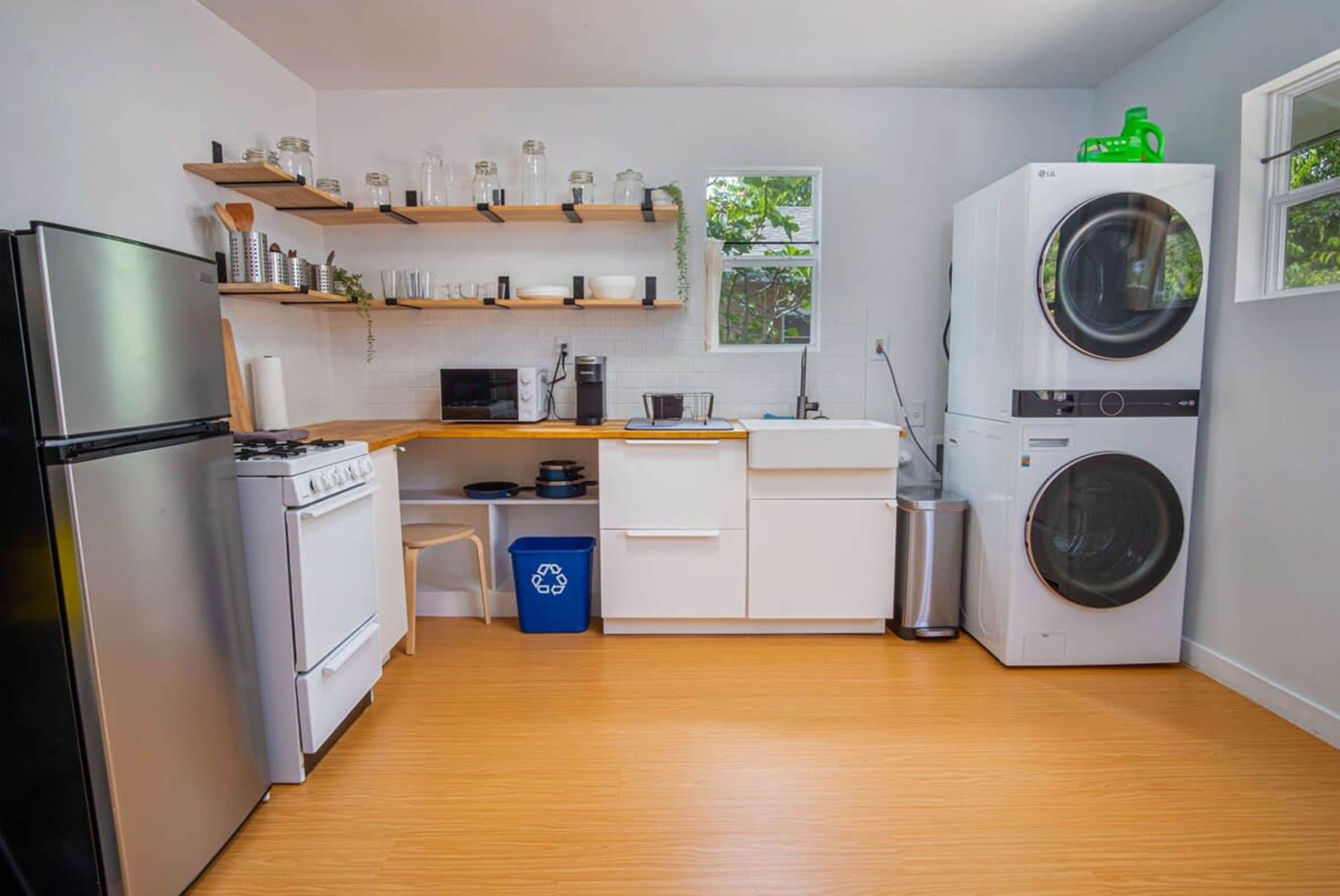 A compact kitchen with white cabinets, a stainless steel refrigerator, a stove, a microwave, and a double-door washing machine.