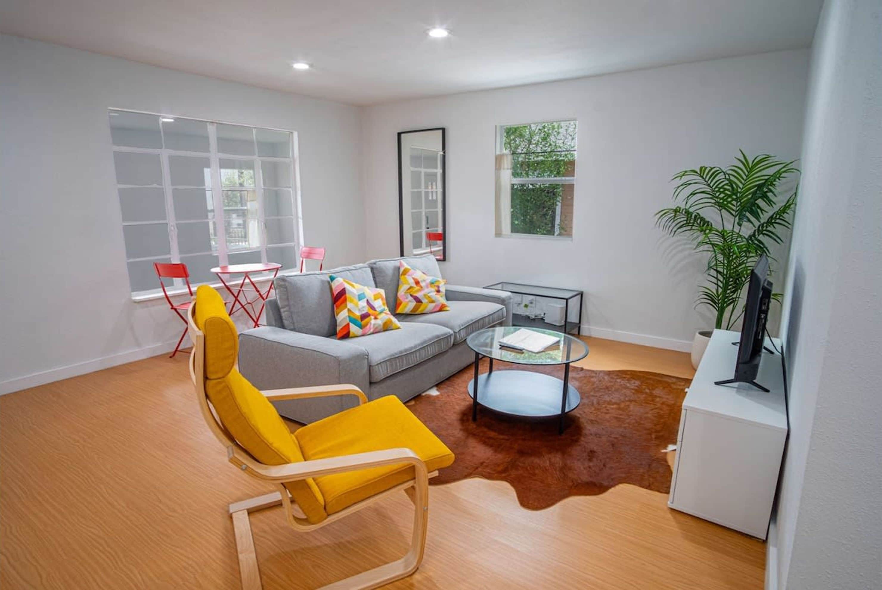 A modern living room with a grey sofa, yellow armchair, glass coffee table, and a white TV stand.