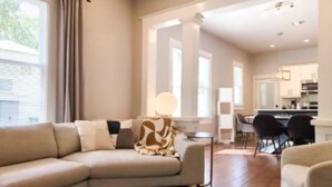 A modern living room with a beige sofa, a patterned rug, and a dining area with chairs and a table. - Chic Downtown Farmhouse With Garden and BBQ Grill (San Antonio)
