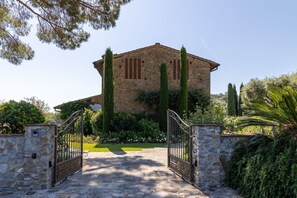 A stone building with a central tower, surrounded by greenery and a paved entrance.