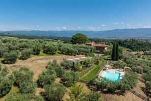 An olive grove with a stone house, a swimming pool, and a view of distant mountains.