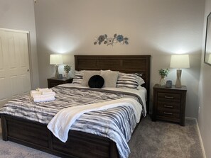 Ein ordentlich bezogenes Bett mit einer gestreiften Tagesdecke, zwei Nachttische mit Lampen und eine an der Wand befestigte Blumendekoration.