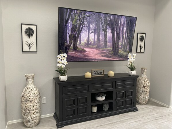 Ein modernes Wohnzimmer mit einem großen Flachbildfernseher an der Wand, einem dunklen Holz-Konsolentisch mit Dekoration und zwei großen gewebten Vasen.