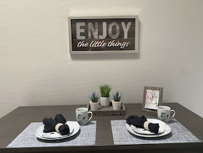 A dining table with two plates, two black napkins, two white mugs, and two small potted plants.