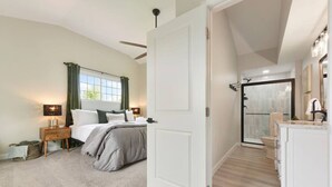 Un dormitorio con cama, mesita de noche, lámpara y vistas al baño.